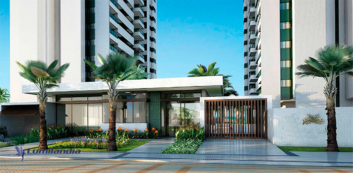 Iluminação Prédios e Condomínios entrada de um prédio residencial moderno, com dois prédios brancos visíveis. Há um portão de acesso de madeira escura e uma portaria com teto branco horizontal e grandes janelas de vidro. A área externa é ajardinada, com grama verde, palmeiras altas nas laterais e caminhos de pedra ou azulejo.